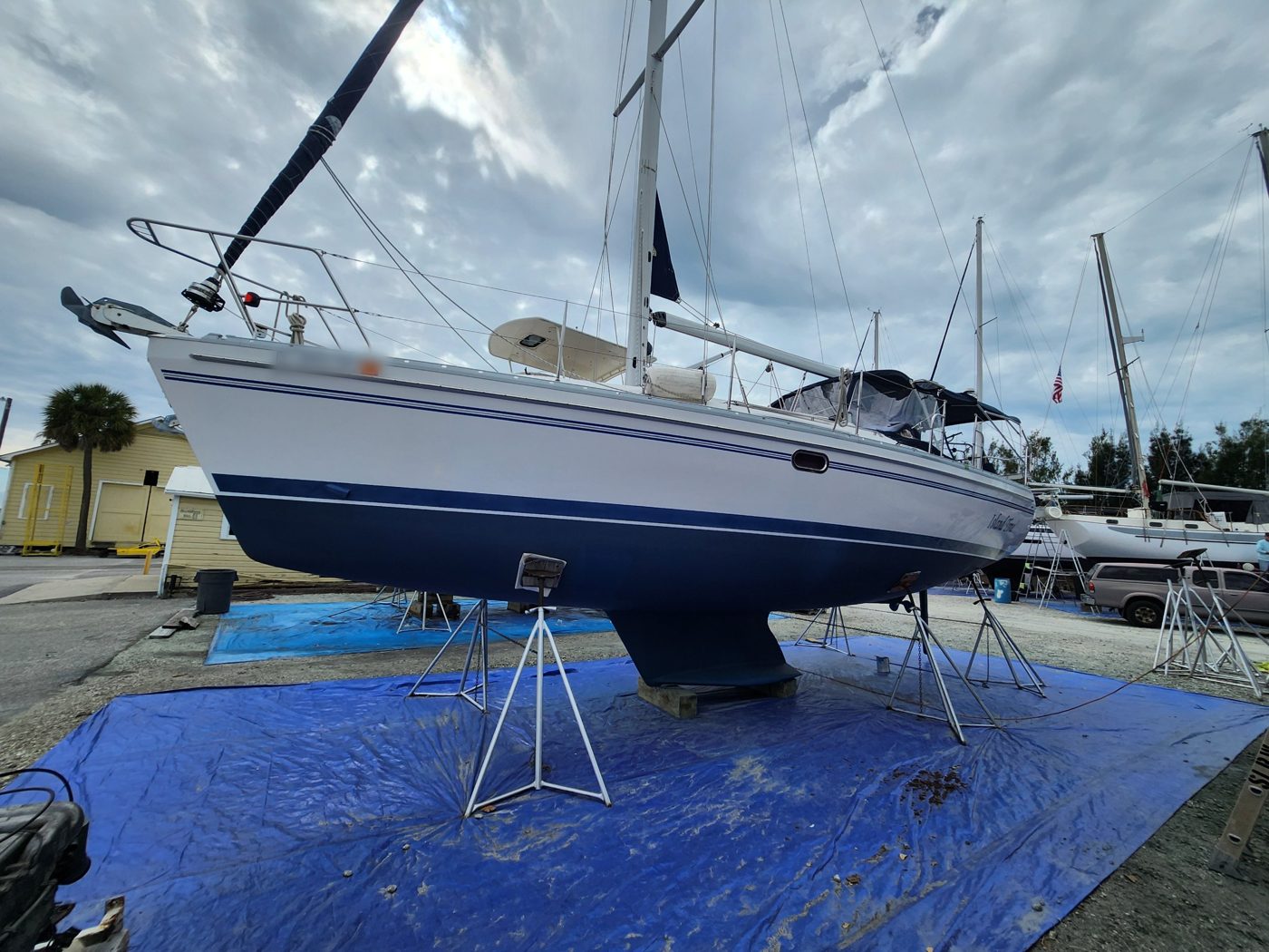 A blue-hulled sailboat on stands in a Florida boatyard, freshly painted